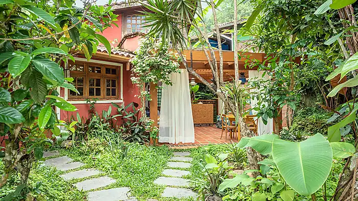 Jardim da pousada com o caminho de pedra até a varanda da casa vermelha