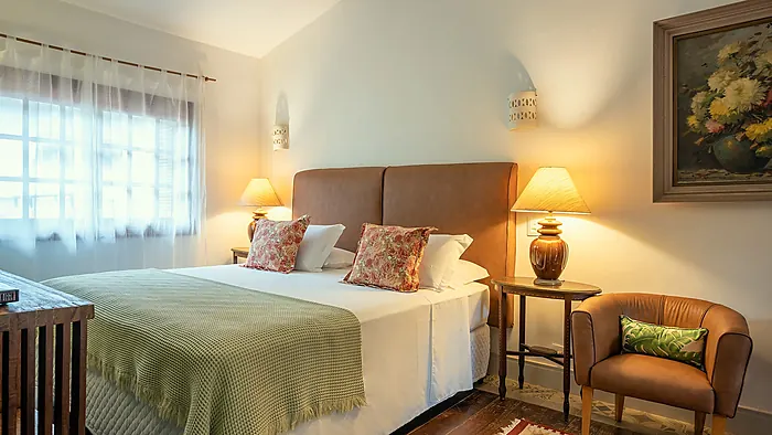 Quarto da Casa Linda Camburi com cama de casal, abajures e poltrona de couro